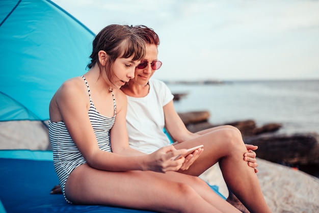 Mãe e filha usando telefone inteligente na praia