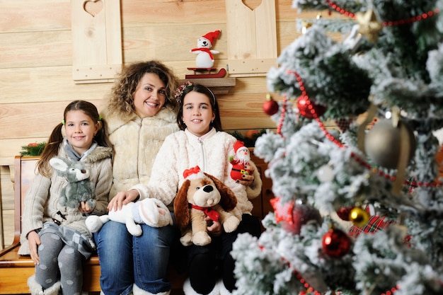 Foto mãe e filhas com presentes perto de uma árvore de natal