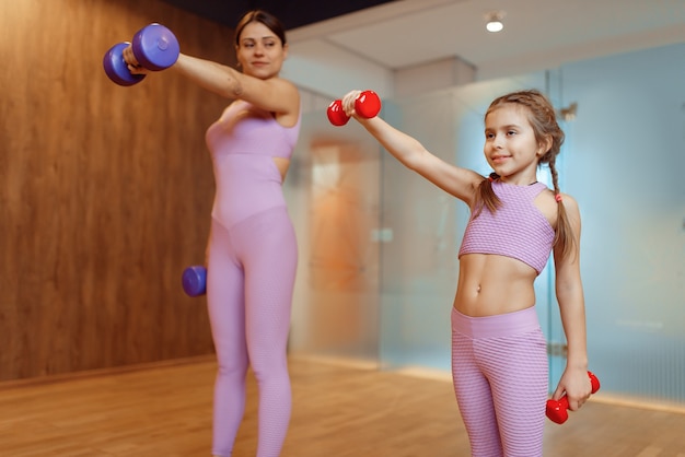 Mãe e filhas fazendo exercícios com halteres no ginásio, treino de fitness. Mãe e filha em roupas esportivas, treinamento conjunto em clube de esporte