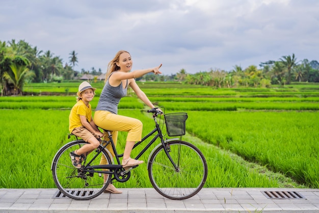 Mãe e filho andam de bicicleta em um campo de arroz em ubud bali viajam para bali com conceito de crianças