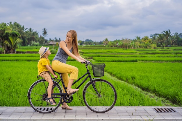 Mãe e filho andam de bicicleta em um campo de arroz em Ubud Bali Viaje para Bali com o conceito de crianças