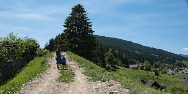 Mãe e filho andando na estrada rural Caminhada no campo em um dia ensolarado Céu azul colinas e floresta