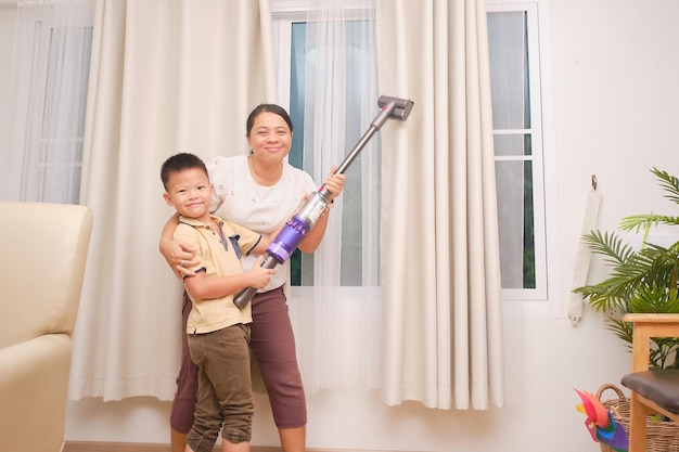 Foto mãe e filho asiáticos se divertindo enquanto limpavam a sala junto com aspirador de pó em casa