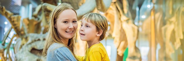 Mãe e filho assistindo esqueleto de dinossauro em formato longo de banner de museu