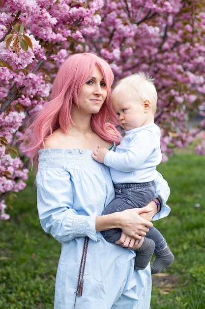 Mãe e filho bebê se divertindo no parque primavera perto da árvore florescendo de sakura rosa conceito de primavera