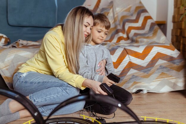 Mãe e filho brincam de corrida no tapete em casa se divertem e se abraçam Mãe solteira cria seu filho brincando de carros