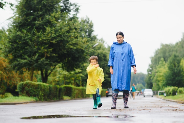 Mãe e filho brincando na chuva, usando botas e capa de chuva