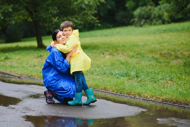 Mãe e filho brincando na chuva, usando botas e capa de chuva