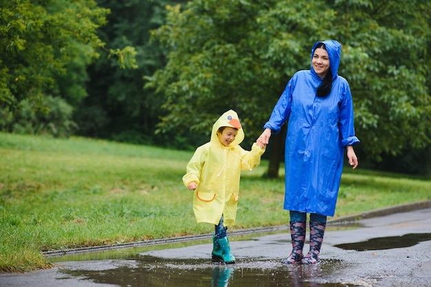 Mãe e filho brincando na chuva, usando botas e capa de chuva