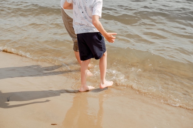 Mãe e filho caminhando na praia. água fria do mar. caminhe descalço pela praia.