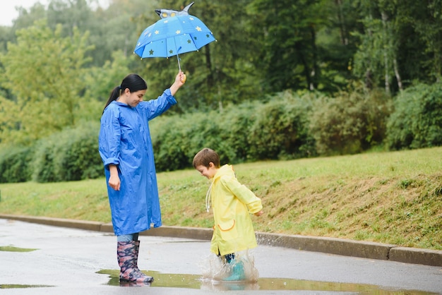 Mãe e filho caminhando no parque na chuva usando botas de borracha