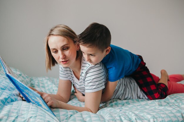 Mãe e filho caucasianos felizes família lendo livro no quarto mãe e menino criança passando tempo