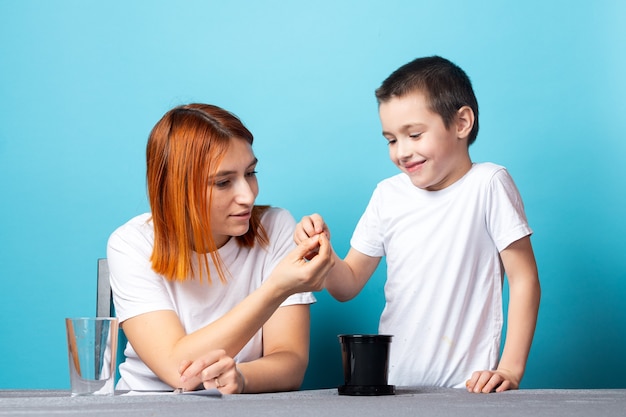 Mãe e filho colocam terra em um vaso preto para plantar uma semente e cultivar uma planta doméstica na mesa