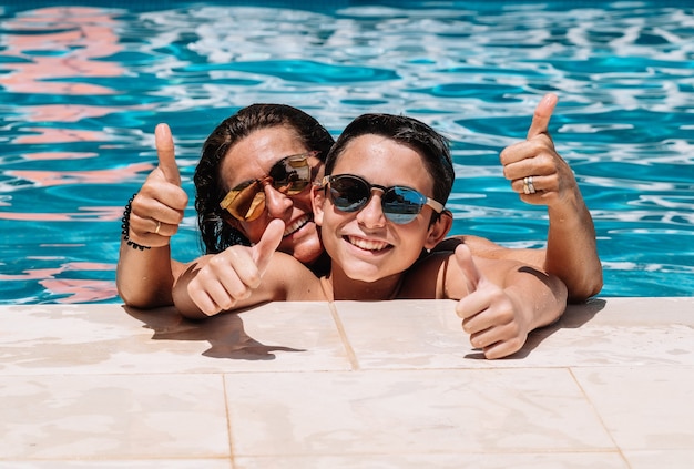 Mãe e filho com óculos escuros estão encostados na beira da piscina em um dia ensolarado de verão