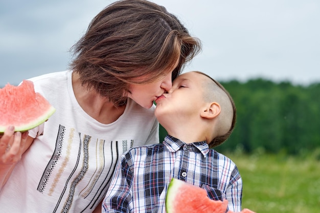 Mãe e filho comendo melancia no prado ou parque Família feliz no retrato ao ar livre do piquenique Menino e mãe