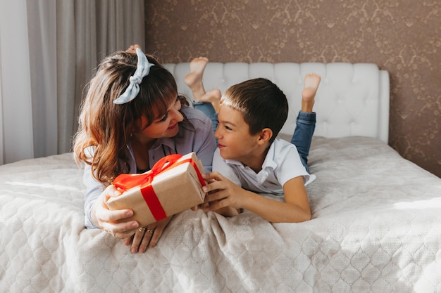 Mãe e filho deitam-se na cama. criança dá a sua mãe um presente para o dia das mães.