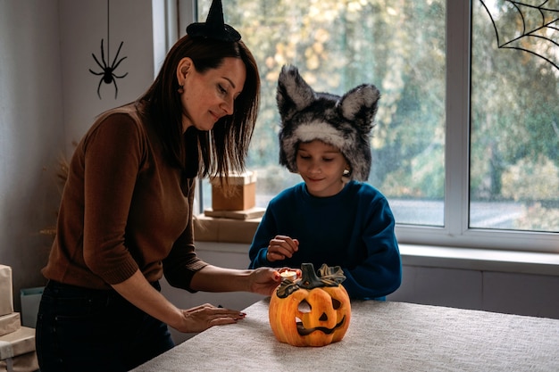 Mãe e filho em fantasias de halloween brincam juntos com a lâmpada de abóboras assustadoras jackolantern em casa