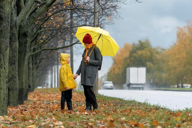 Mãe e filho estão andando na chuva no parque outono, perto da rodovia. Outono sombrio