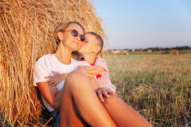 Mãe e filho estão descansando em um palheiro em um campo ao pôr do sol família feliz abraçando e beijando amor e ternura