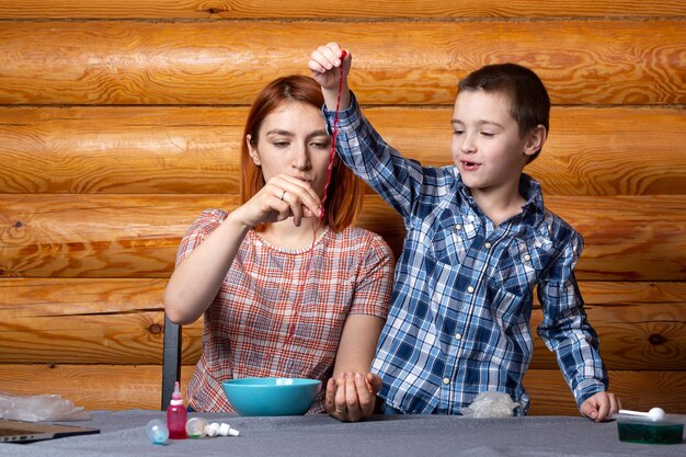 Mãe e filho estão fazendo experiências químicas fazendo vermes poliméricos multicoloridos na mesa