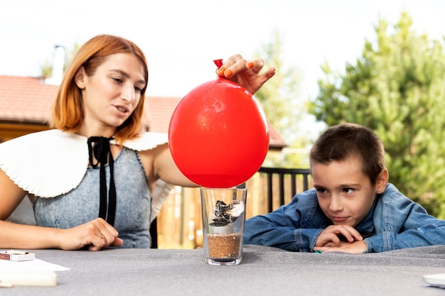 Mãe e filho estão fazendo experimentos físicos em casa. Uma experiência com uma criança sobre qual das bolas está vazia ou com água vai estourar mais rápido com o fogo. Passo 4