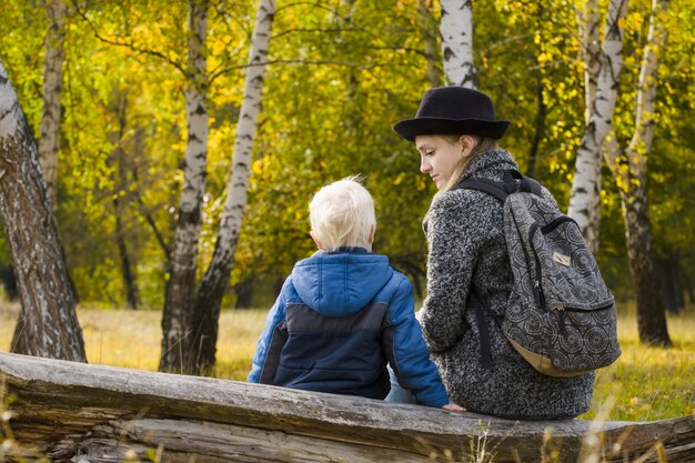 Mãe e filho estão sentados na floresta de outono em um log