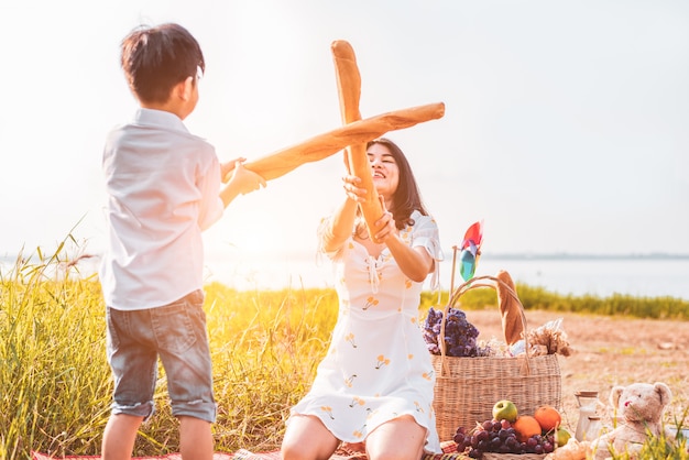 Mãe e filho jogam esgrima com pão juntos quando piquenique ao ar livre perto do lago ou rio