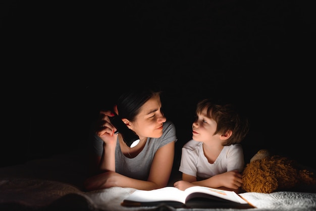 Mãe e filho lendo um livro com uma lanterna debaixo do cobertor