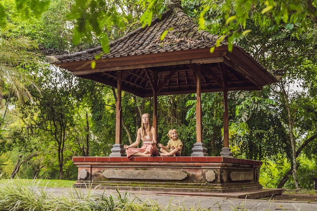 Mãe e filho meditam praticando ioga no gazebo tradicional de Bali