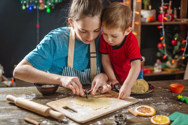 Mãe e filho moldam a massa para assar pão de mel caseiro de Natal