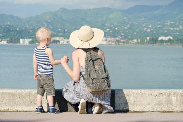 Mãe e filho no cais no fundo do mar, farol e montanhas ao longe