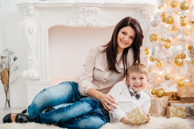 Mãe e filho no estúdio de natal. retrato de mãe feliz e filho sentado perto da árvore de natal.