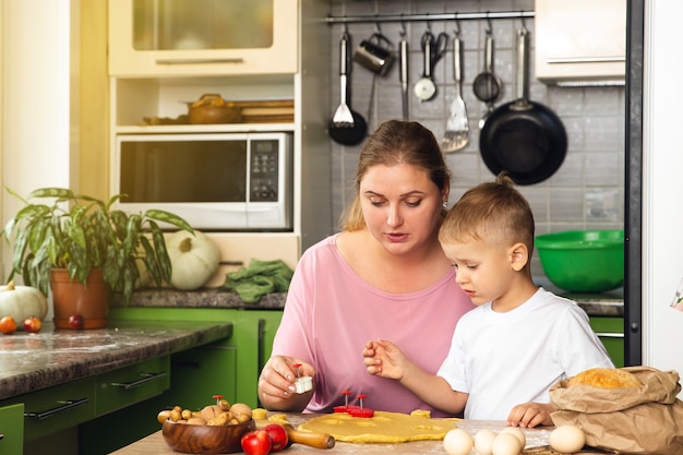 Mãe e filho pequeno em idade pré-escolar preparam biscoitos, mãe sorridente e amorosa aprendem a cozinhar com o filho pequeno, fazendo o almoço no fim de semana na cozinha juntos