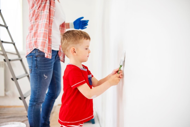 Mãe e filho pintam a parede com tinta usando rolo e pincel