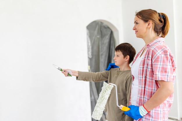 Mãe e filho pintam a parede com tinta usando rolo e pincel