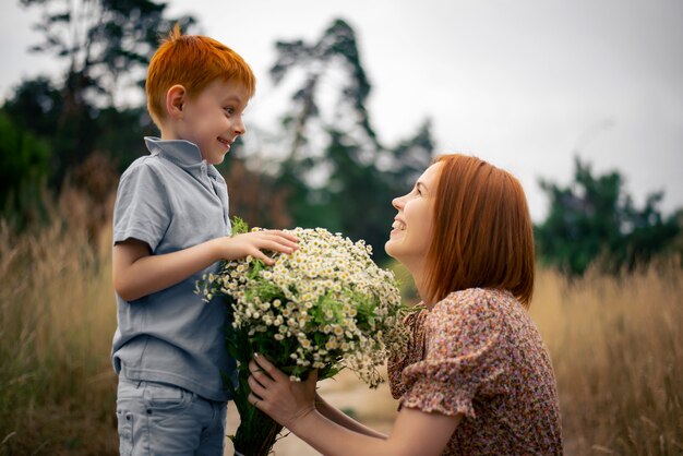 Mãe e filho ruivos com um grande buquê de flores silvestres na natureza no verão