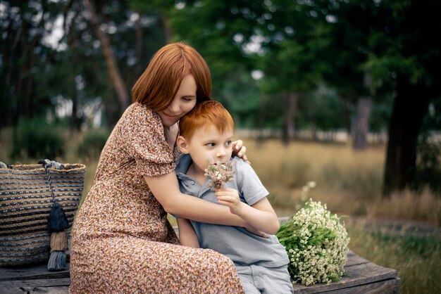 Mãe e filho ruivos com um grande buquê de flores silvestres na natureza no verão