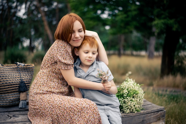 Mãe e filho ruivos com um grande buquê de flores silvestres na natureza no verão