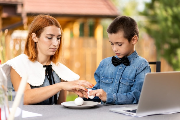 Mãe e filho se divertem e batem ovos na manhã de páscoa. páscoa para toda a família. divirta-se enquanto se prepara para a páscoa.