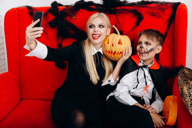 Mãe e filho se divertem no sofá vermelho e fazem um close de selfie. Emoção e Halloween