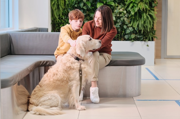 Mãe e filho sentados no sofá com o cachorro e esperando a visita ao veterinário na clínica