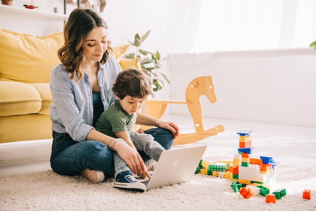 Mãe e filho sentados no tapete e usando laptop