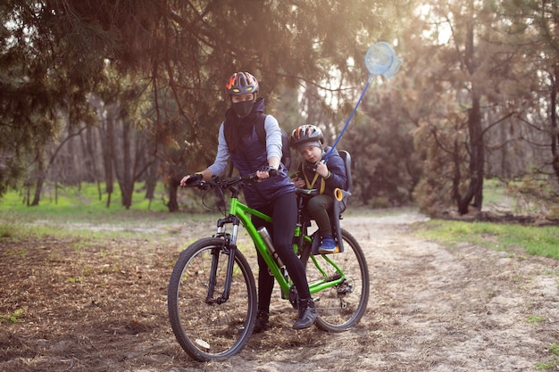 Mãe e filho usando capacetes andam de bicicleta na floresta