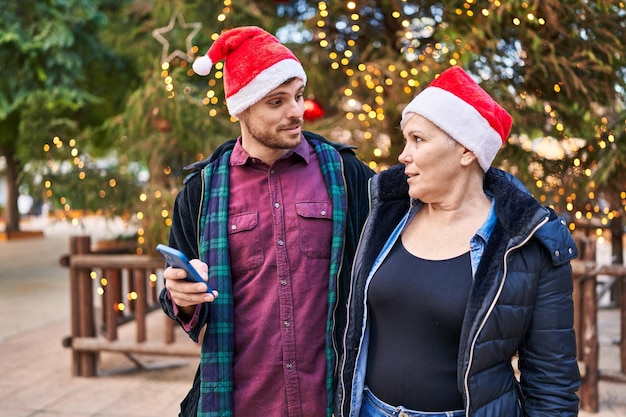 Mãe e filho usando chapéu de natal usando smartphone no parque