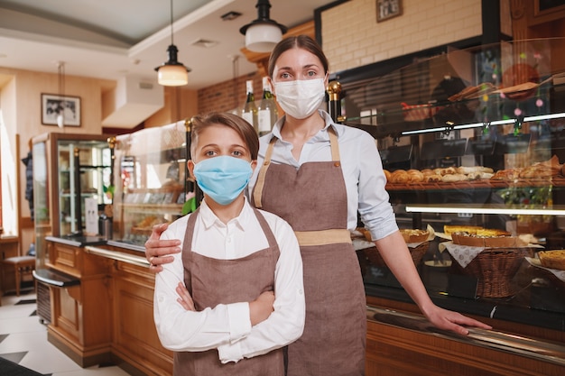 Mãe e filho usando máscaras médicas, trabalhando na padaria da família