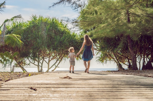 Mãe e filho vão para as férias de resort de praia no mar no caminho de praia tropical para a praia