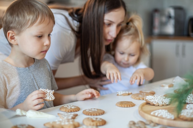 Mãe e filhos decoram pão de mel de natal em casa um menino e uma menina pintam com cornetas com açúcar.