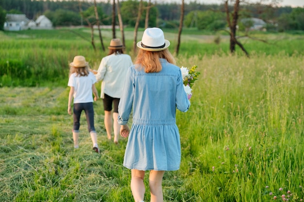 Mãe e filhos duas filhas caminhando ao longo de uma estrada rural através de um prado. Verão, natureza, família, férias