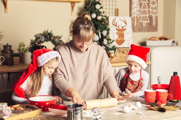 Mãe e filhos estão preparando biscoitos na cozinha. Decorações de Natal, tradições familiares, comida de Natal, vésperas de férias.