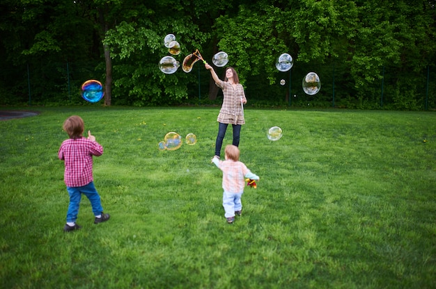 Mãe e filhos jogando bolhas de sabão no gramado verde no parque.